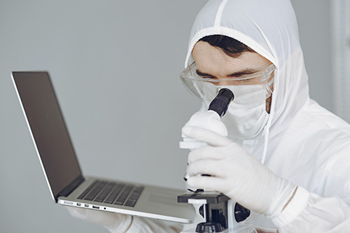 Man holding a computer and inspecting microscope